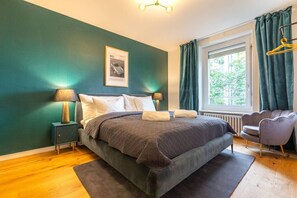 Een slaapkamer met een bed, nachtkastjes, een raam met gordijnen en een stoel.