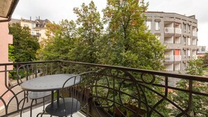 Un balcon avec une table et des chaises, entouré d’arbres et d’immeubles.