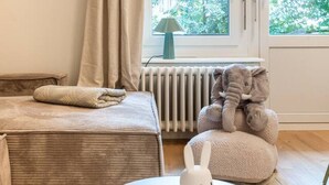 Een slaapkamer met een bed, een radiator, een raam met gordijnen, een lamp en een pluche olifant speelgoed.