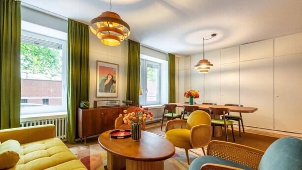 A modern living room with a sofa, dining table, chairs, and a coffee table. There is a picture on the wall and a window with curtains. - Vintage 2-BR in central Zürich · sleeps 5 (Zürich)