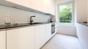 A modern kitchen with white cabinets, a black countertop, and a window with a view of greenery. - Vintage 2-BR in central Zürich · sleeps 5 (Zürich)