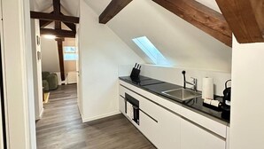 Une cuisine moderne dotée d’une lucarne, de meubles blancs et d’une poutre en bois au plafond.
