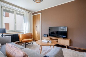 Un salon moderne avec un canapé, un fauteuil et une table basse. Un téléviseur est fixé au mur, et un meuble est placé en dessous.