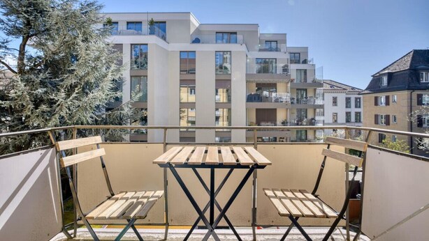 Un balcon doté d’une table et de chaises en bois, d’où l’on peut admirer une rangée d’immeubles d’appartements modernes.