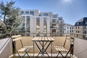 Un balcon doté d’une table et de chaises en bois, d’où l’on peut admirer une rangée d’immeubles d’appartements modernes.