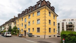 Un immeuble résidentiel à plusieurs étages, doté d’une façade jaune, de nombreuses fenêtres et d’un toit plat.