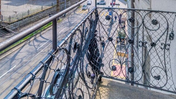 En balkong med utsikt över en stadsgata, ett metallstaket och en byggnad med klassisk arkitektur.