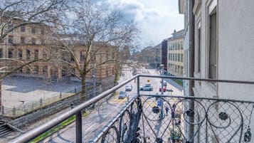 A balcony with a view of a city street, a metal fence, and a building with classical architecture.