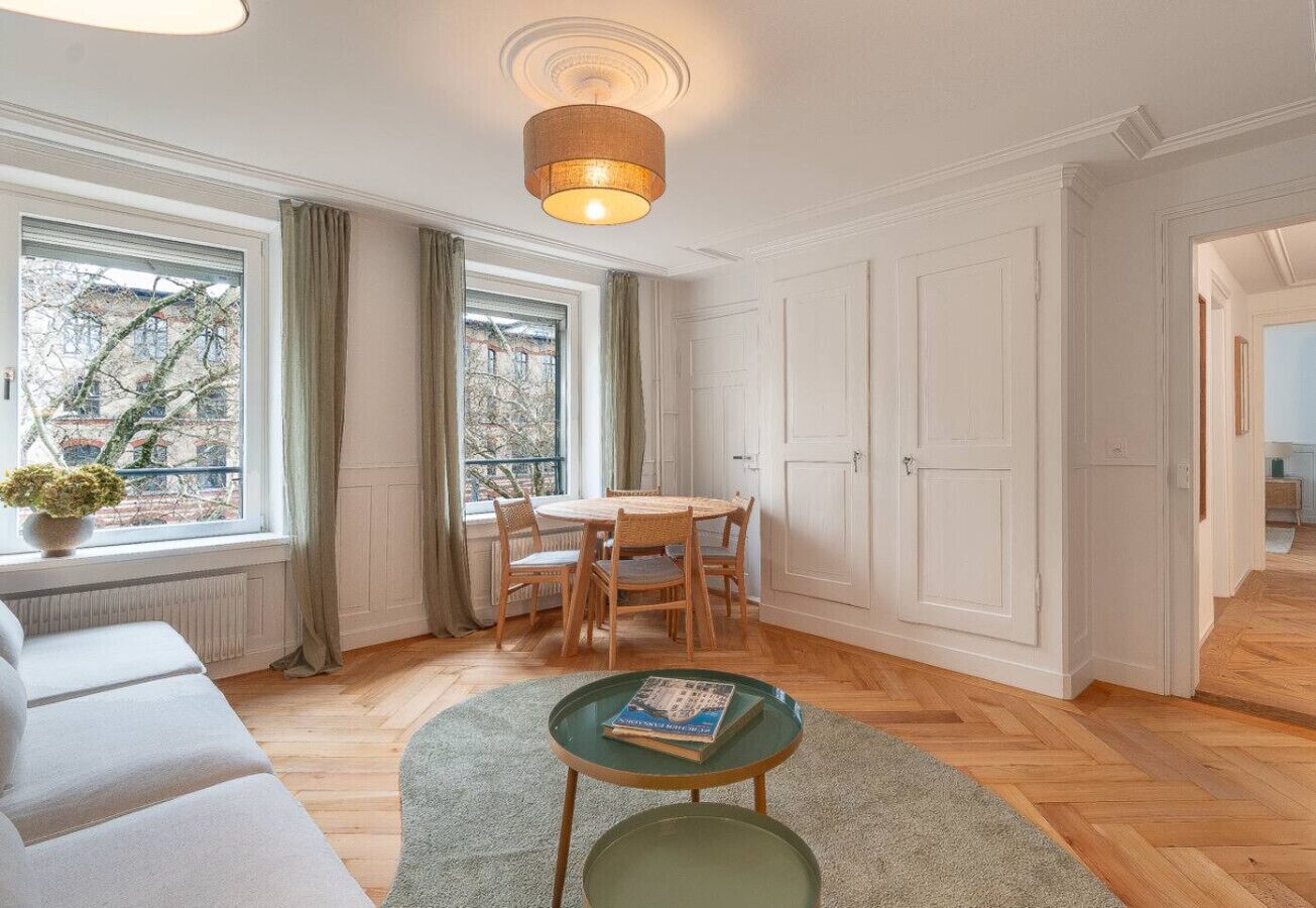Un salon moderne avec un canapé, une table ronde entourée de chaises, une petite table verte et un luminaire suspendu.