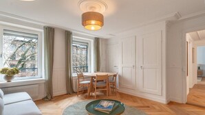 Ett modernt vardagsrum med en soffa, ett runt bord med stolar, ett litet grönt bord och en hängande lampa.
