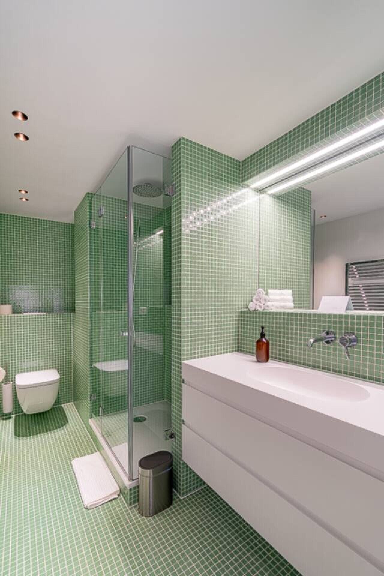 Une salle de bain moderne avec des carreaux verts à motifs à carreaux, une douche en verre, un lavabo blanc et un miroir.