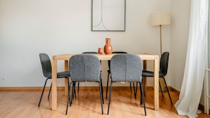 Ein Essbereich mit einem Holztisch, vier grauen Stühlen, zwei Terrakotta-Vasem und einem modernen, abstrakten Gemälde an der Wand.