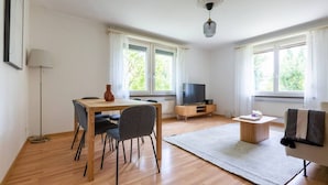 Ein modernes Wohnzimmer mit einem Holzesstisch, zwei Stühlen, einem Fernsehschrank und einem Sofa.
