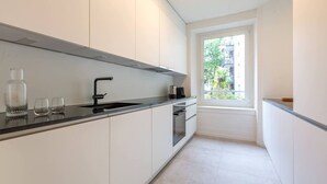 A modern kitchen with white cabinets, a black countertop, and a window providing a view of greenery outside. - Stylish 3-BR design flat with terrace · Kreis 6 (Zürich)