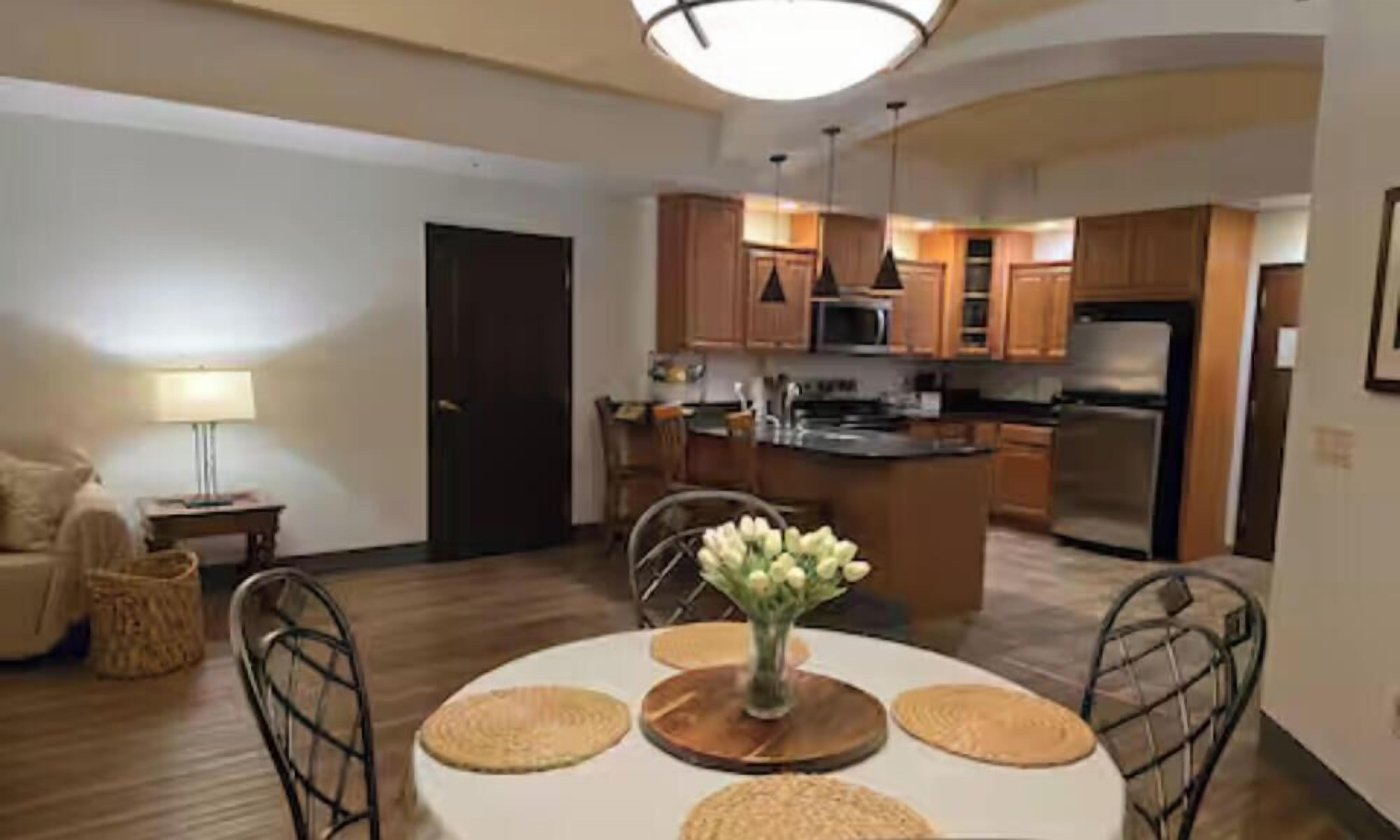 A modern kitchen with wooden cabinets, a central island, and a dining area with a round table and placemats.