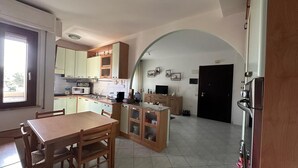 A compact kitchen with a dining area, featuring a wooden table and chairs, a built-in oven, and a microwave. - Poetto Casa Bach Ck, Cozy apartment a few steps from the sea (Quartu Sant'Elena)