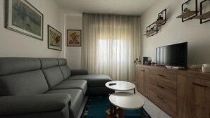 A modern living room with a grey sofa, a small white table, a TV, and a wooden cabinet. - Poetto Casa Bach Ck, Cozy apartment a few steps from the sea (Quartu Sant'Elena)