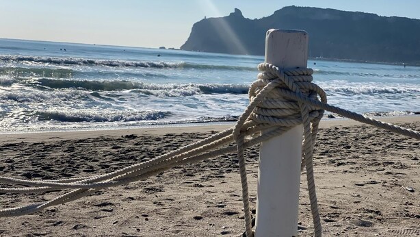 A rope tied to a post on a sandy beach with waves and a distant mountain. - Poetto Casa Bach Ck, Cozy apartment a few steps from the sea (Quartu Sant'Elena)