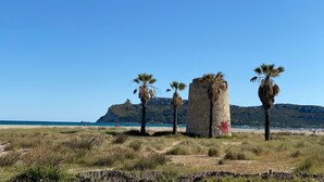 A coastal landscape with a stone structure, palm trees, and a beach in the background. - Poetto Casa Bach Ck, Cozy apartment a few steps from the sea (Quartu Sant'Elena)