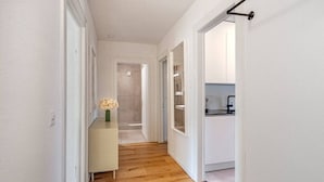 Un couloir étroit avec un plancher en bois, des murs blancs et une petite table sur laquelle est posé un vase de fleurs.