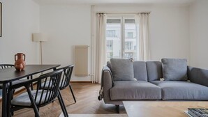 Ett modernt vardagsrum med en grå soffa, ett matbord med stolar, en golvlampa och ett element.