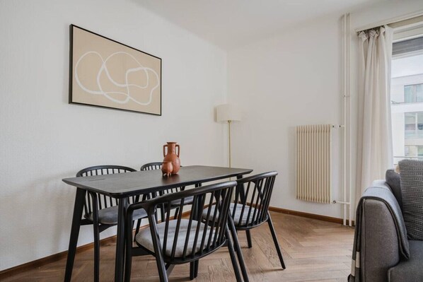 Een eethoek met een tafel, stoelen, een vaas, een vloerlamp en een radiator.