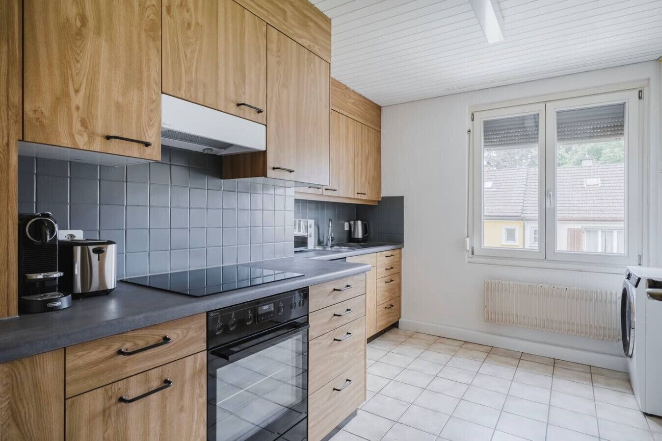 Une cuisine moderne avec des meubles en bois, un plan de travail noir et une fenêtre équipée de stores.