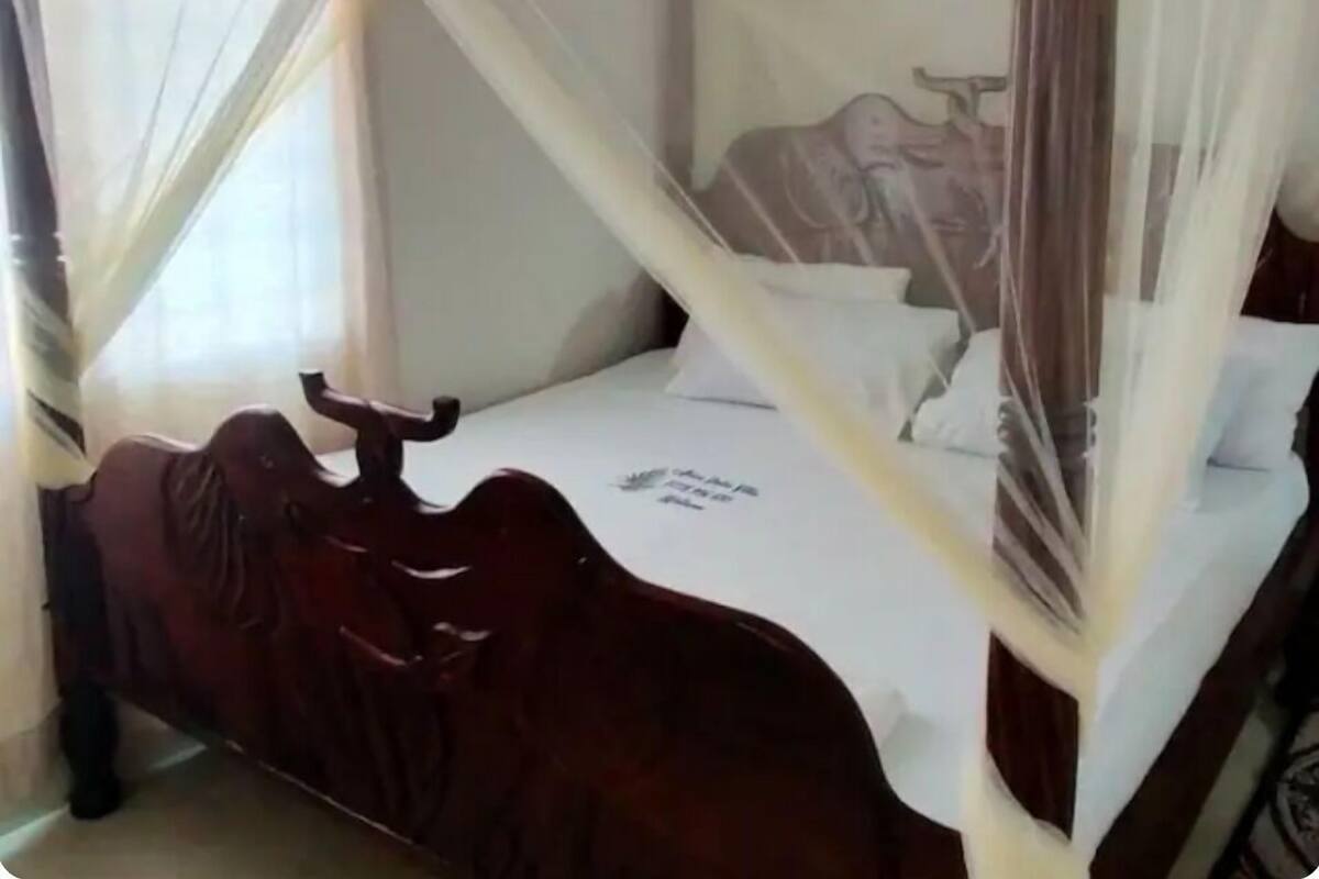 Un lit à baldaquin, avec une tête de lit en bois et une table de chevet fixée au mur.