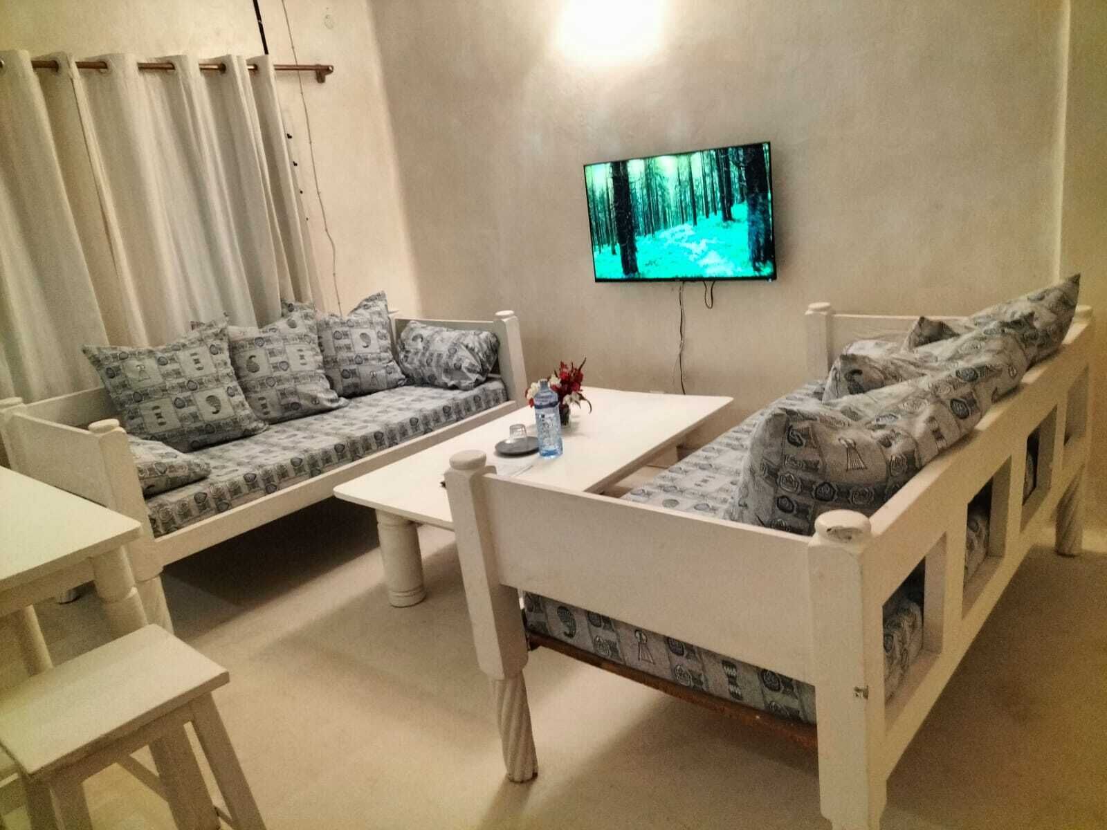 A living room with a sofa set, a coffee table, and a flat-screen TV mounted on the wall.