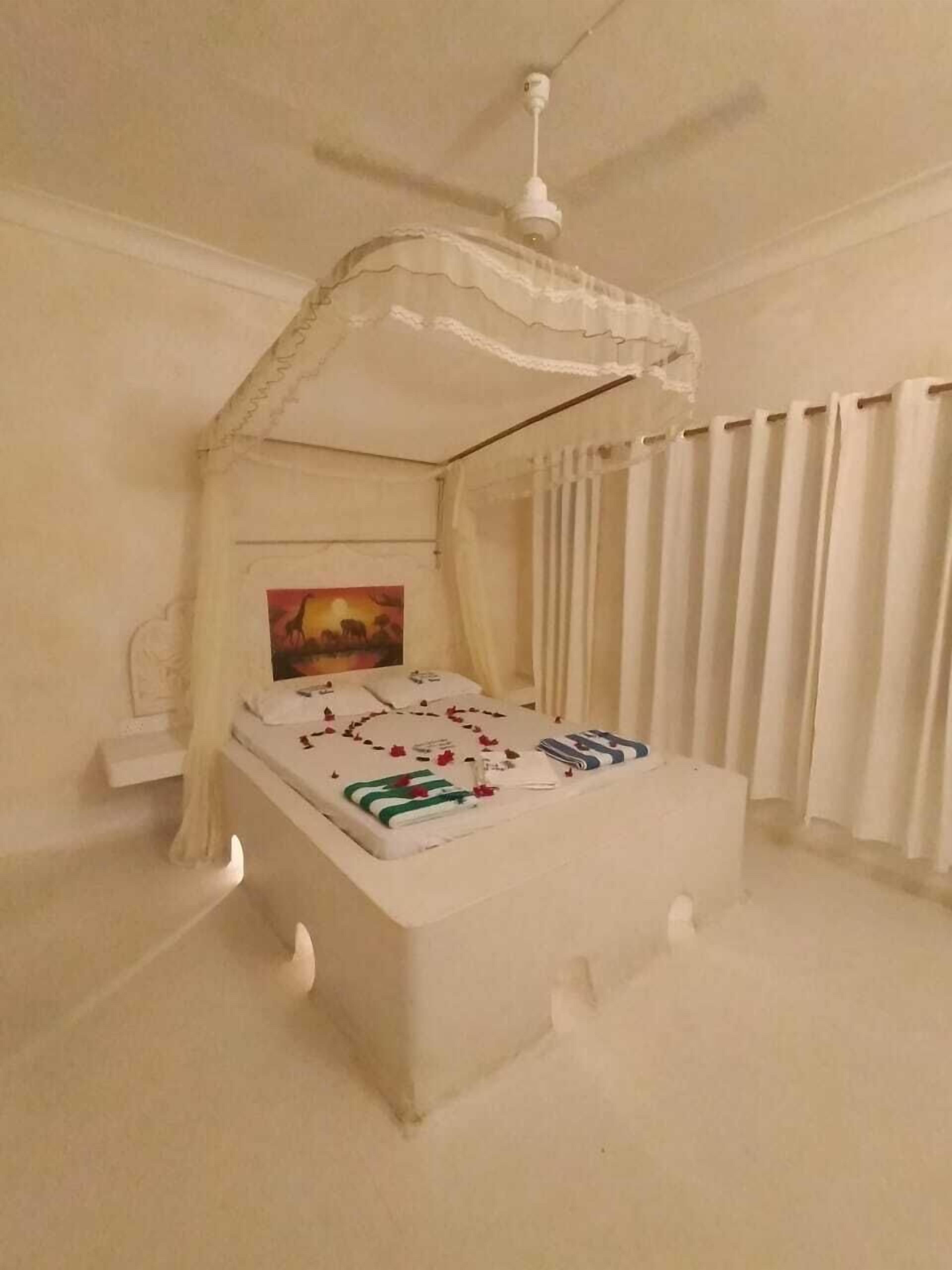 A bedroom with a canopy bed, a painting on the wall, and a window with curtains.