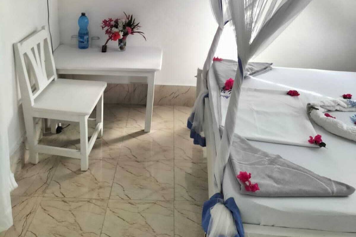 Une pièce comprenant un lit, un bureau, une chaise, un téléviseur et un vase de fleurs.