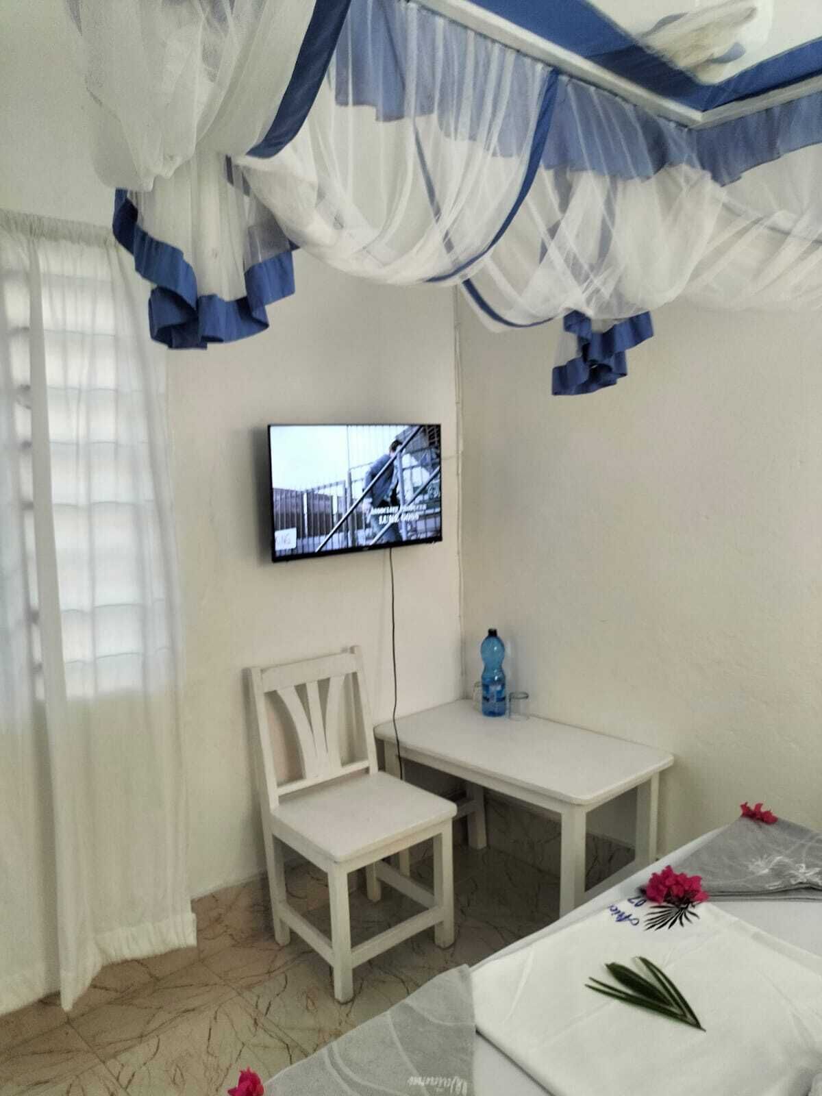 Une petite pièce simple, avec un lit, une chaise, une table et un téléviseur fixé au mur.