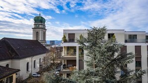 A modern building with a green dome and a clock tower in the background. - Bright 3-BR in Wipkingen — rooftop views, free parking & garden (Zürich)