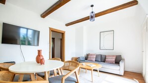 A modern living room with a round dining table, wooden chairs, a sofa, and a television mounted on the wall. - Bright 3-BR in Wipkingen — rooftop views, free parking & garden (Zürich)