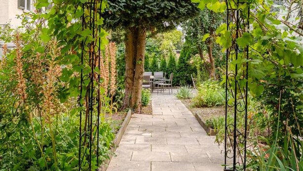 A garden pathway with a pergola structure, surrounded by lush greenery and a stone-tiled path. - Bright 3-BR in Wipkingen — rooftop views, free parking & garden (Zürich)