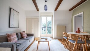 A modern living room with a grey sofa, a round coffee table, and a dining area with wooden chairs and a white table. - Bright 3-BR in Wipkingen — rooftop views, free parking & garden (Zürich)