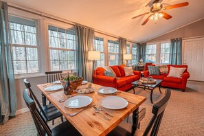 A dining area with a wooden table set for four, a red sofa, and a ceiling fan.
