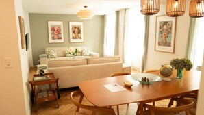 Un coin repas avec une table et des chaises en bois, un canapé à l’arrière-plan et des œuvres d’art accrochées au mur.
