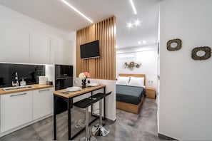 Una cucina moderna con forno integrato, una zona pranzo con tavolo in legno e sgabelli da bar, un letto con copripiumino verde e una TV montata su un pannello di legno.