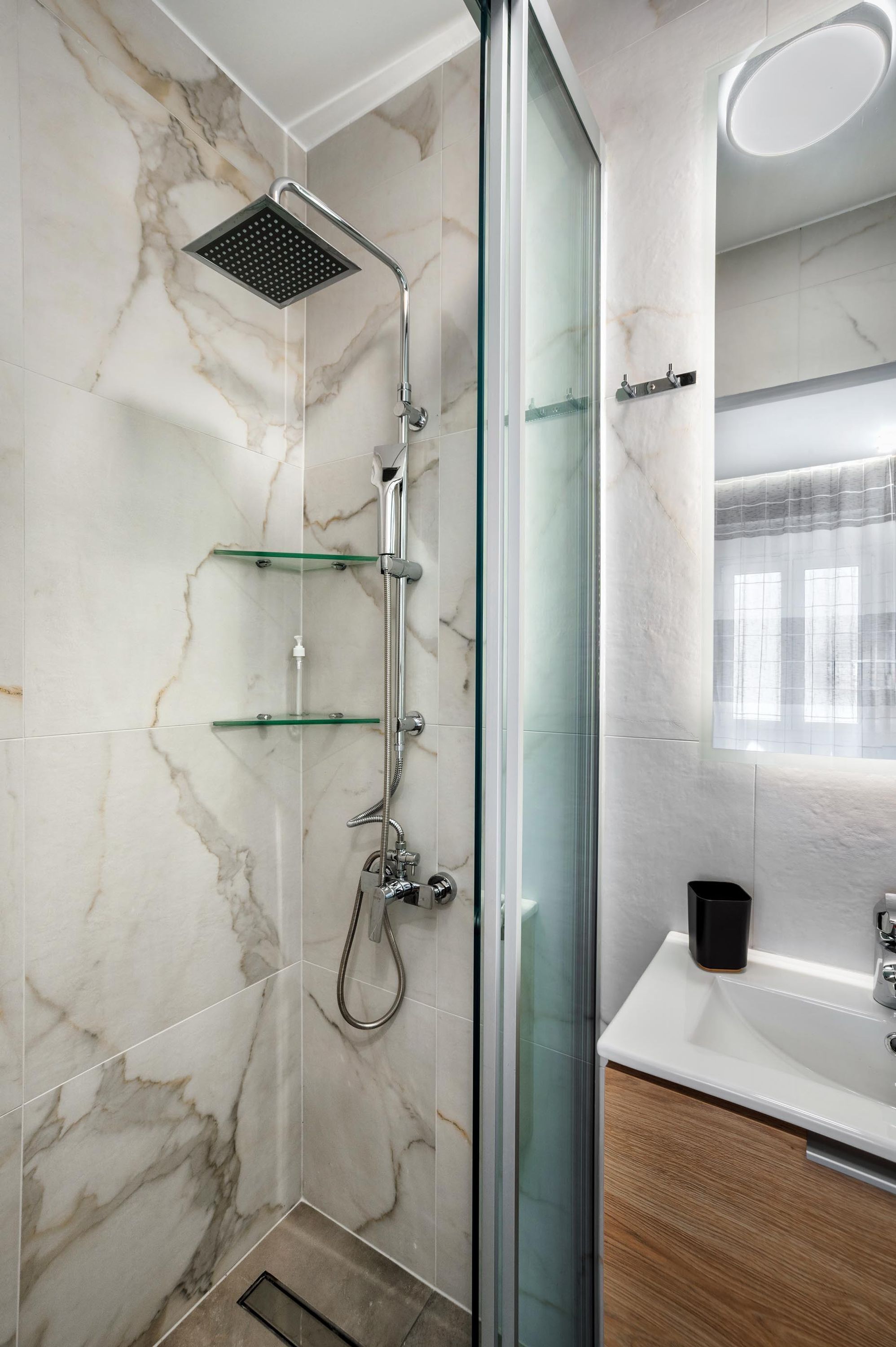 Une salle de bain moderne avec une douche à parois de verre, des murs en marbre et un meuble-lavabo en bois.
