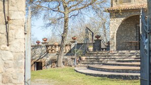 Un bâtiment en pierre avec un escalier menant à une porte, entouré d’herbe et d’arbres.