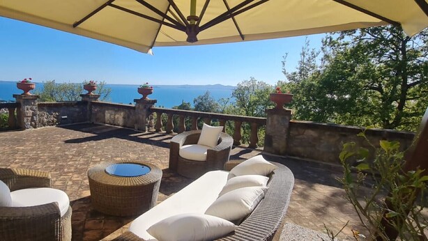 Une terrasse dotée de meubles en osier, d’une table ronde et offrant une vue sur la mer.