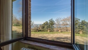 Une pièce dotée d’une grande fenêtre donnant sur un espace verdoyant, avec des arbres, et offrant une vue lointaine sur une étendue d’eau.