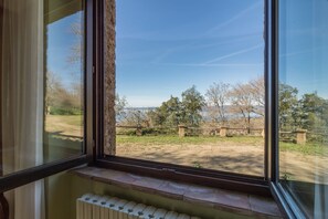 Una habitación con un amplio ventanal que da a un espacio verde con árboles y una vista distante de un cuerpo de agua.