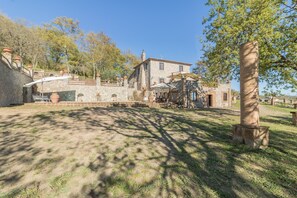 A stone building with a patio area, outdoor seating, and a view of the surrounding landscape. - Il Casale del Sughereto (Bolsena)