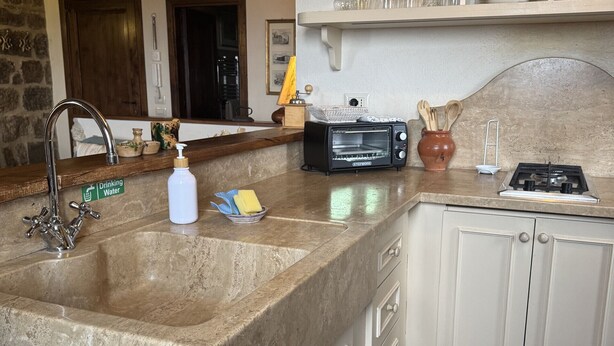 A kitchen with a granite countertop, a built-in sink, white cabinets, a stove, and a ship model on the wall.