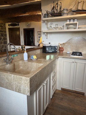 A kitchen with a granite countertop, a built-in sink, white cabinets, a stove, and a ship model on the wall.