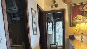 A hallway with wooden flooring, a ceiling fan, a bench, and a door leading to a bathroom.