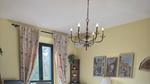 Een gezellige kamer met een bed, een bureau, een stoel, een tafel, een lamp, een kroonluchter en kunstwerken aan de muren.
