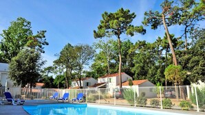 A swimming pool with blue lounge chairs, surrounded by a white fence and trees. - House in Vendee Near Les Conches Beach (Longeville-sur-Mer)